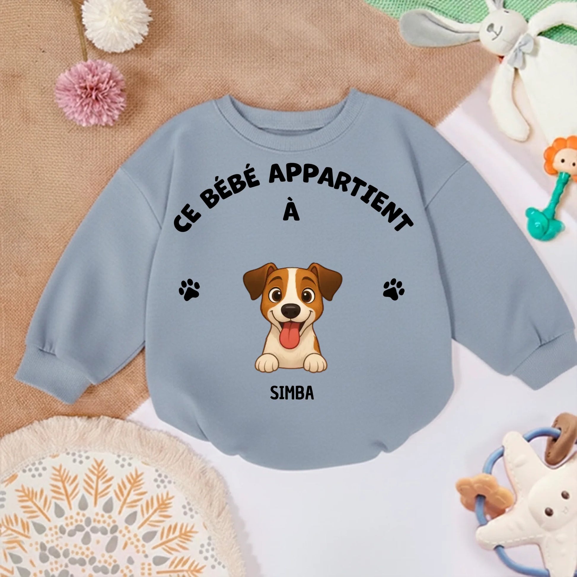 Pull bébé personnalisé posé sur un tapis doux, entouré de jouets, suggérant un usage confortable et ludique à la maison.