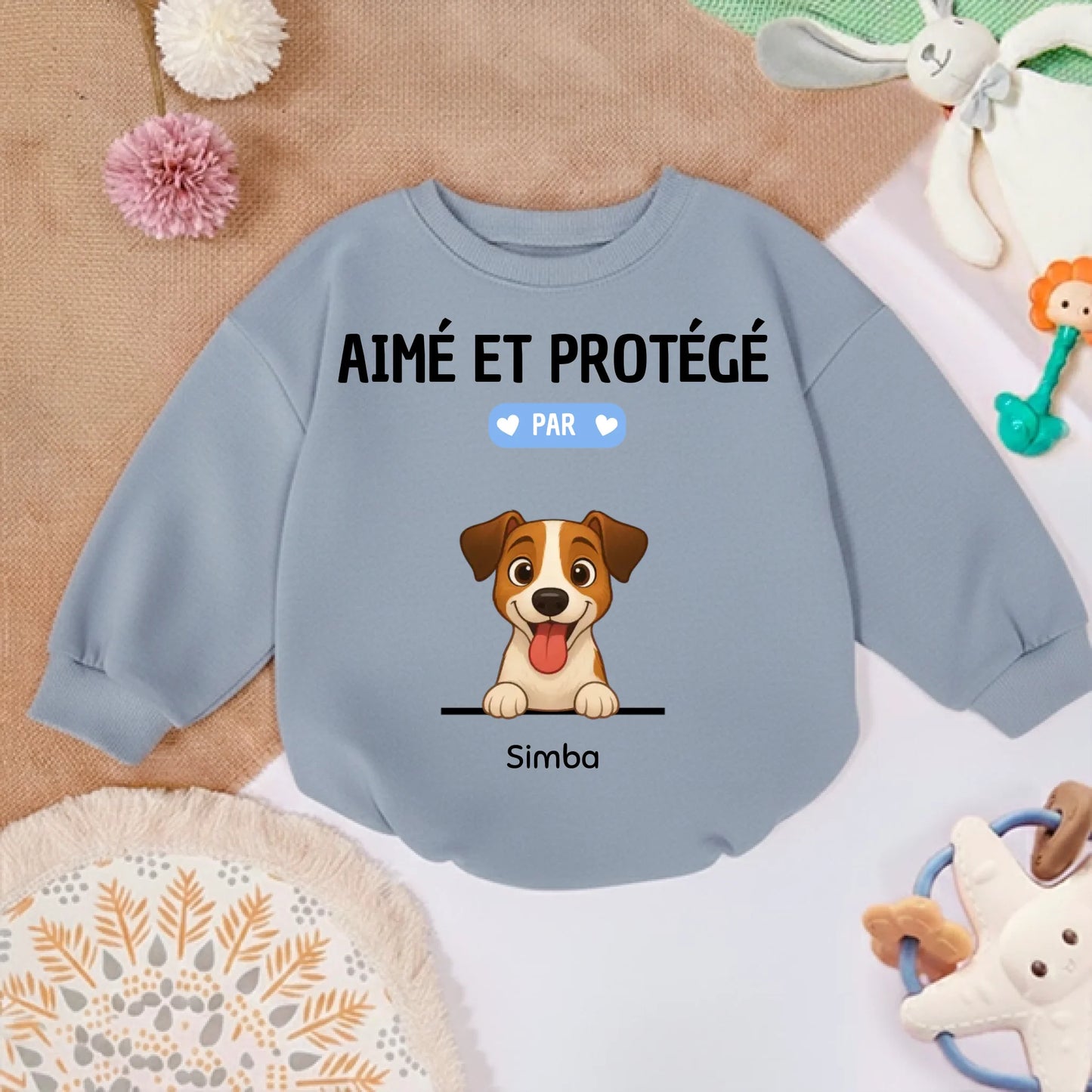 Pull bébé personnalisé posé sur un tapis d'éveil avec des jouets, suggérant un usage quotidien et confortable.