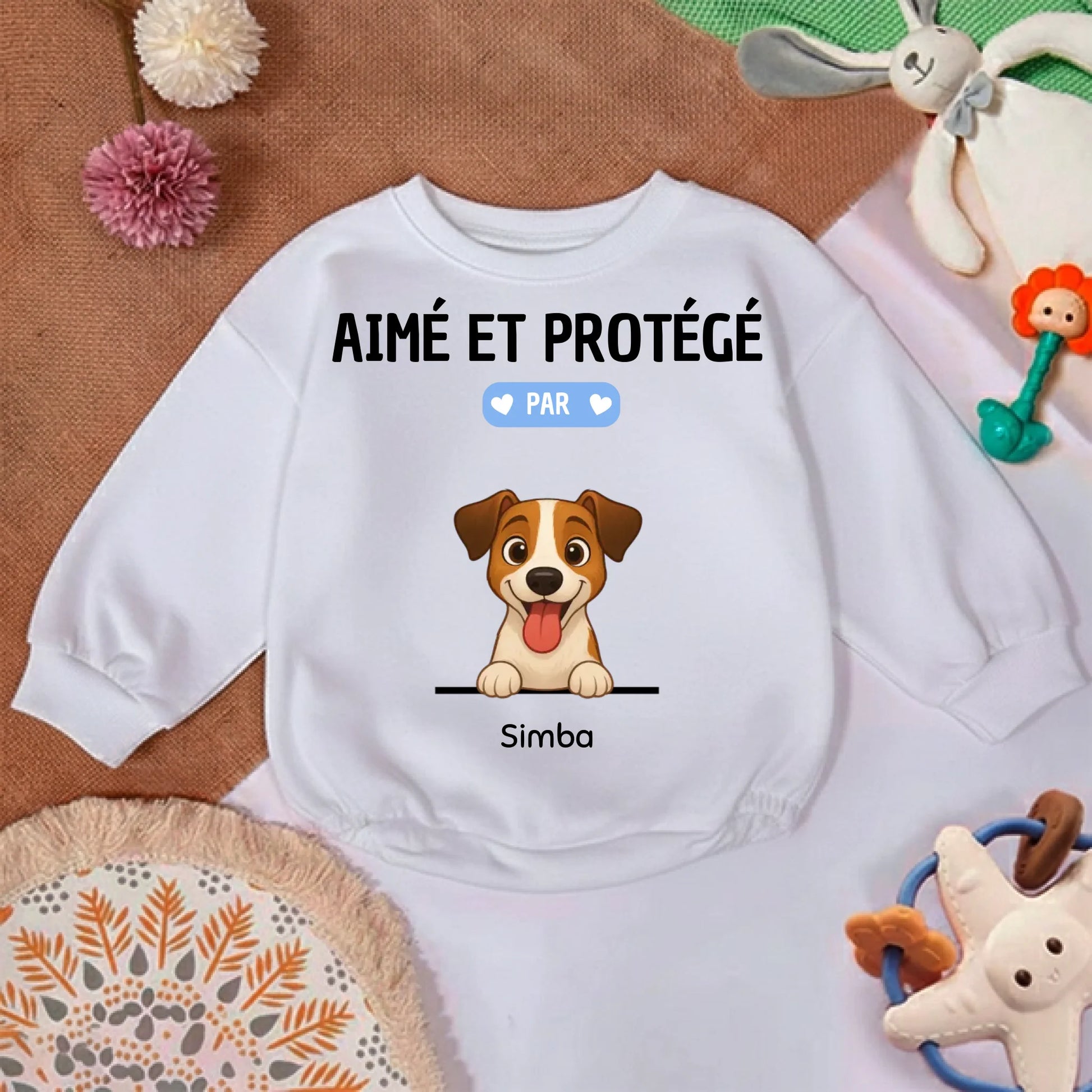 Gros plan sur le motif "Aimé et Protégé par" et l'illustration d'un chiot joyeux sur le pull bébé.
