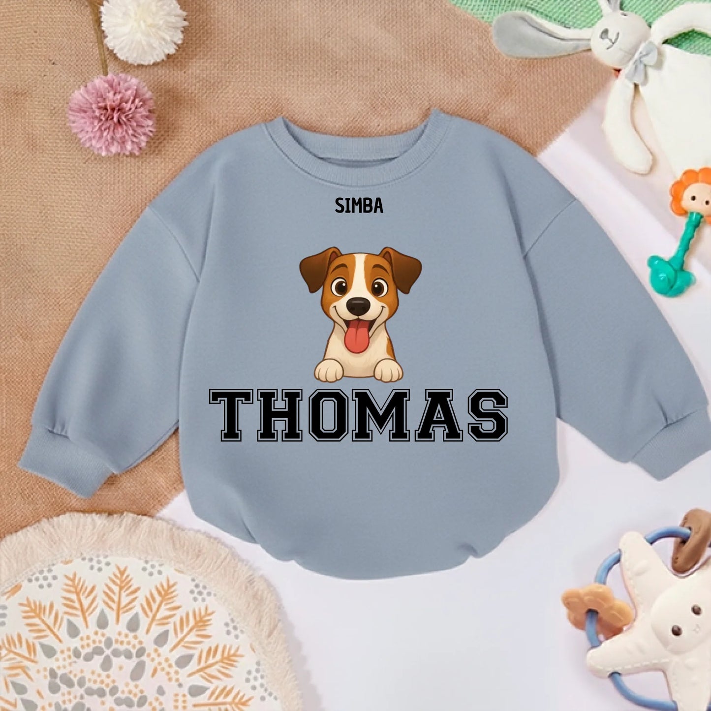 Pull bébé personnalisé posé sur tapis doux avec jouets, ambiance chaleureuse et joyeuse.