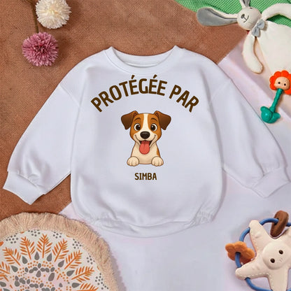 Gros plan sur l'illustration du chien joyeux avec sa langue tirée et le texte 'Protégée par' sur le pull bébé.