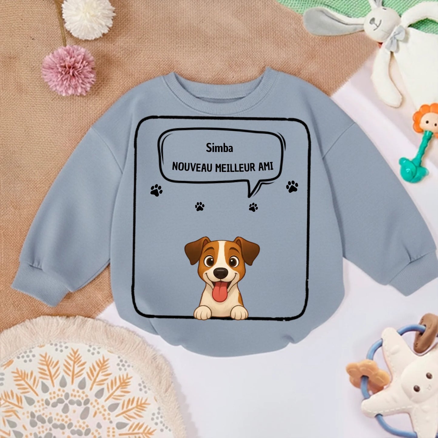 Pull bébé personnalisé posé sur fond doux avec jouets, ambiance chambre d'enfant.