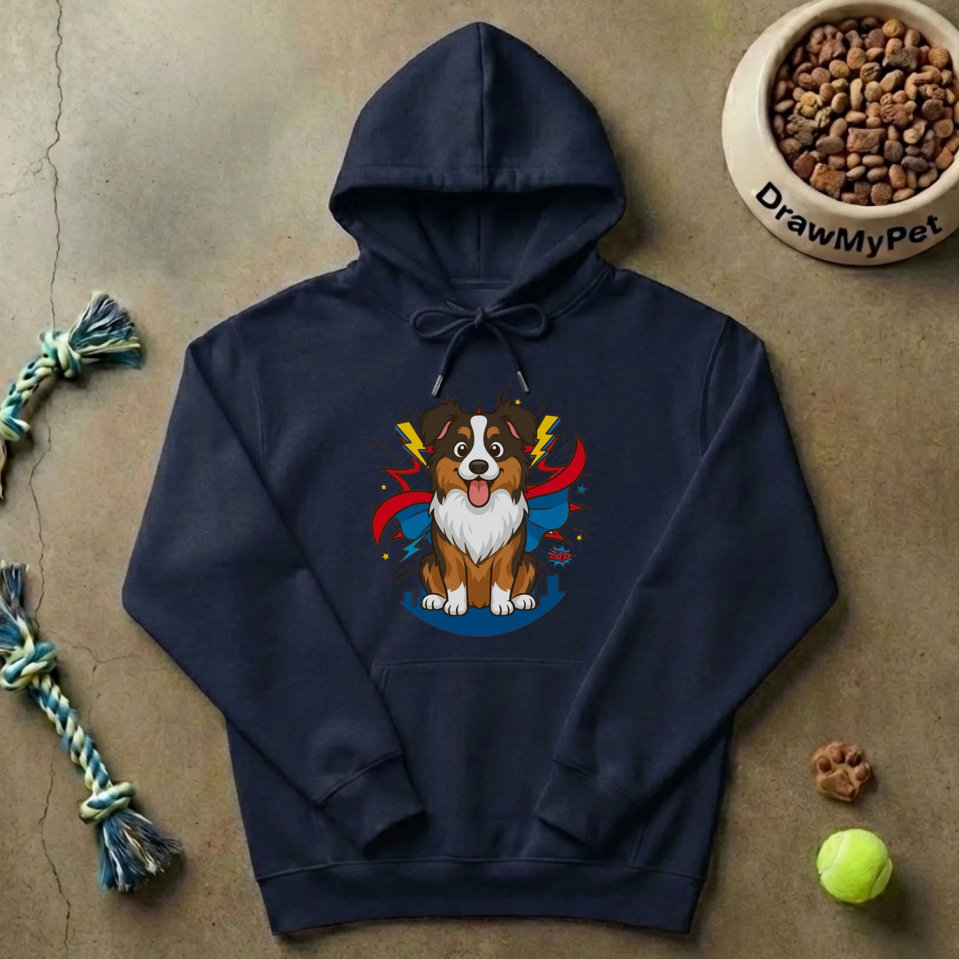 Pull à capuche gris posé au sol, ambiance jeu avec jouet et balle de tennis.