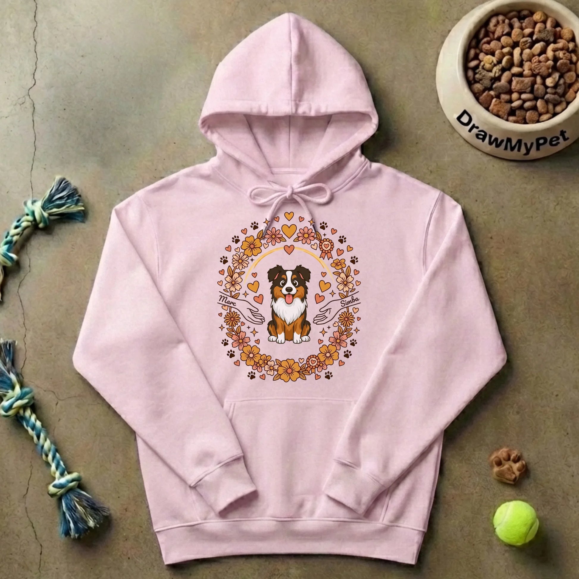 Zoom sur le motif central du pull à capuche gris : un chien tricolore souriant entouré d'une couronne de fleurs, cœurs et pattes, avec des mains et des prénoms personnalisés.