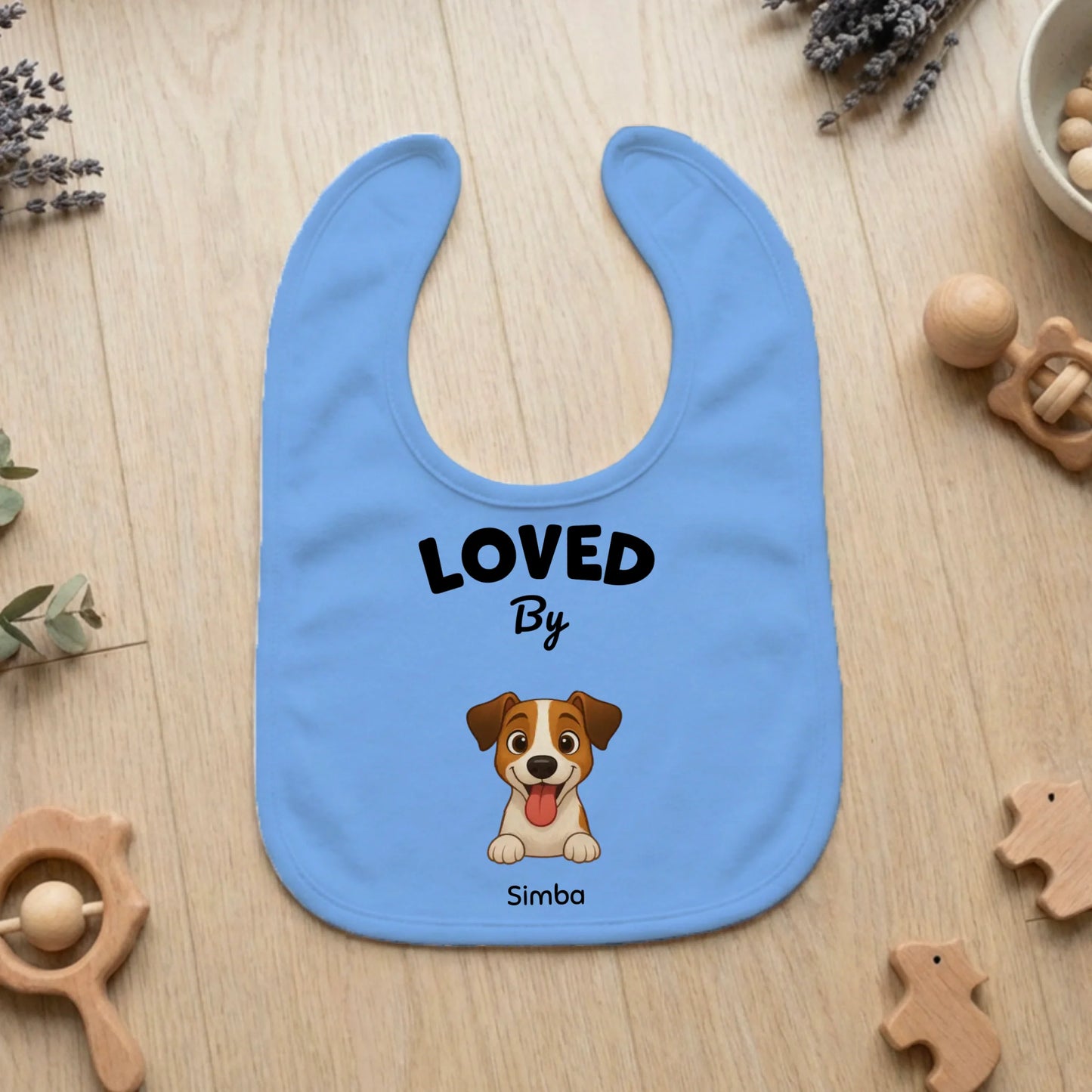 Babero de bebé personalizado azul claro "Loved by Simba" con un dibujo de perro sonriente.