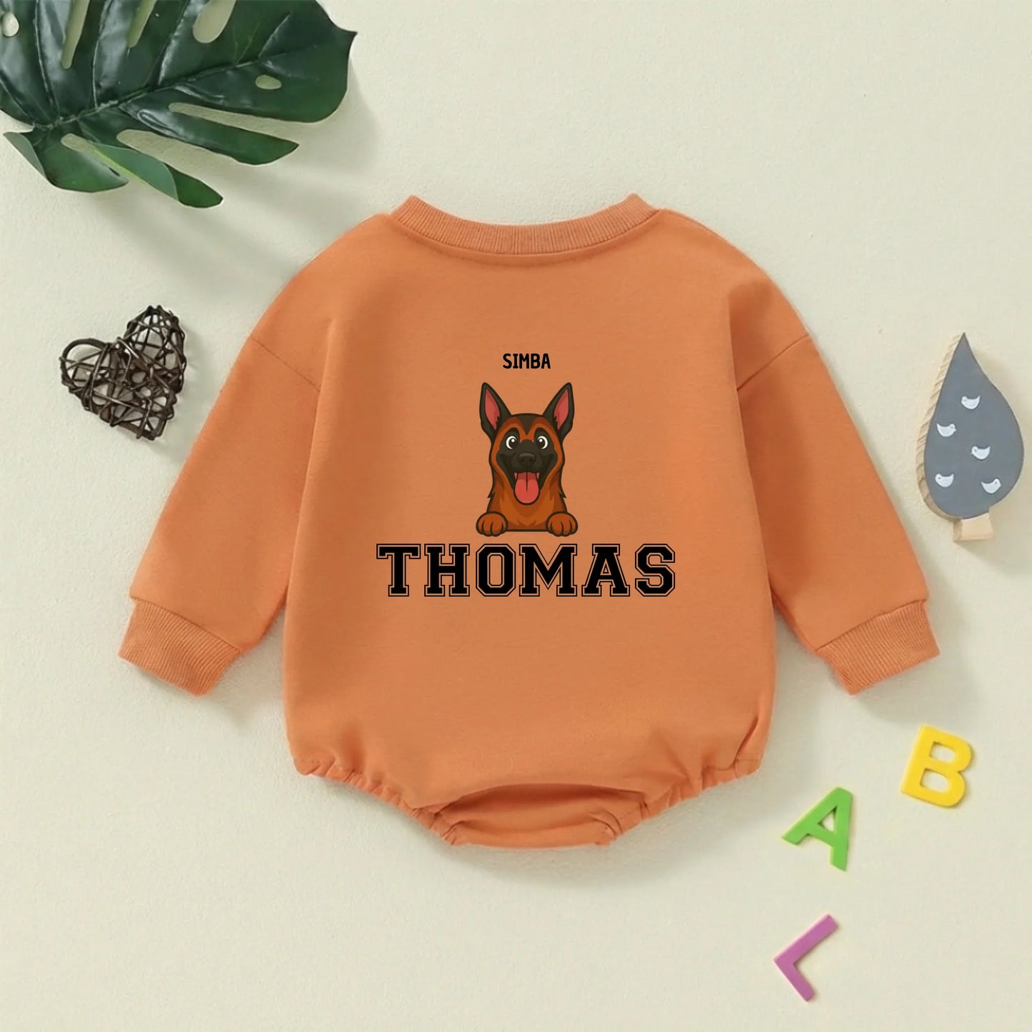 Babyromper met huisdier en babynaam, liggend tussen speelse letters en een Monstera blad