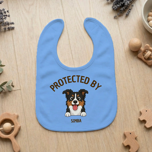 Personalized light blue baby bib with a cartoon tri-color dog and 'Protected By Simba' text.