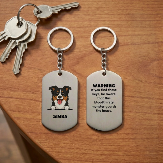 Personalized stainless steel keychain with a cartoon 'bloodthirsty monster' dog and pet name 'SIMBA' next to keys on a wooden table, front view.