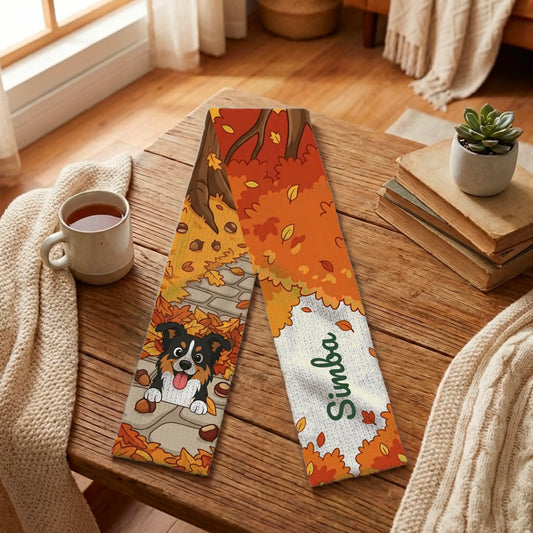 Personalized scarf with a cartoon dog and pet name 'Simba' on an autumn forest walk design, laid on a wooden table with a mug and blanket.